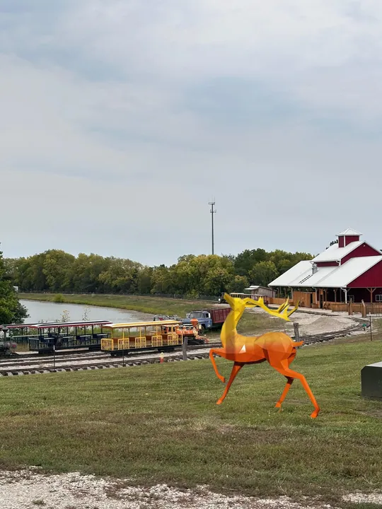 Orange and yellow geometric deer sculpture on a lawn near a train station