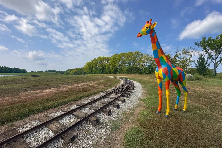 Multicolor patchwork giraffe sculpture beside a railway track