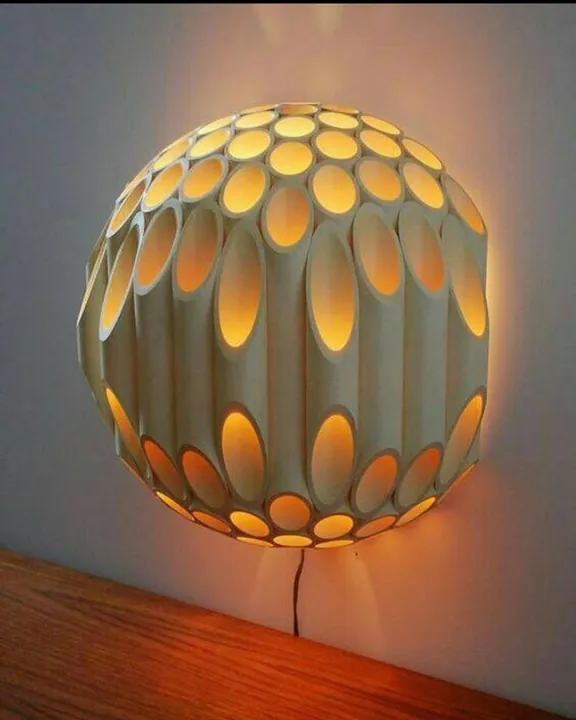 Perforated sphere wall light glowing warm through oval openings