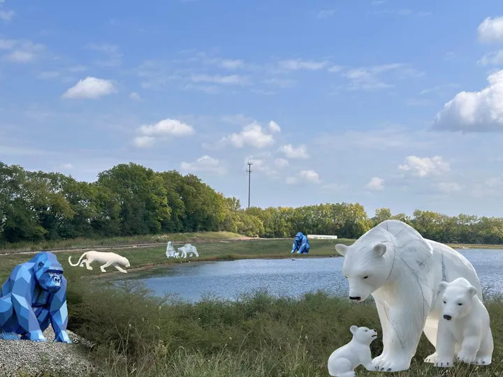 White polar bear family sculptures with blue gorillas along a lake shore