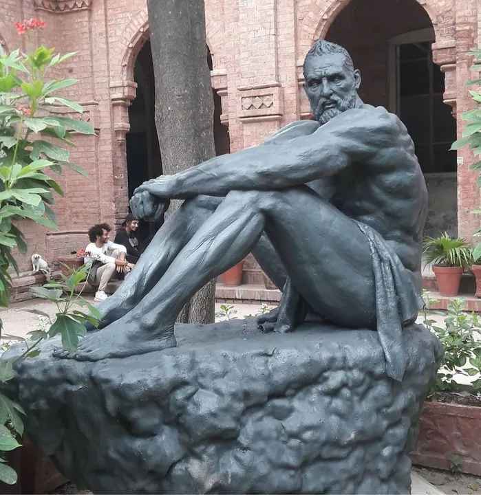 Seated muscular figure sculpture on a carved rock base in a courtyard