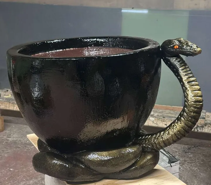 Oversized black cup sculpture with a coiled serpent forming the handle