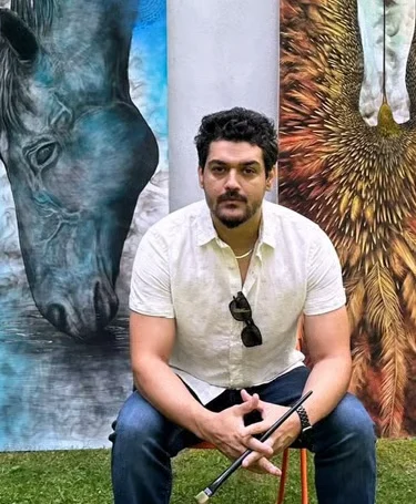 Wazir, sculptor and fine artist at 2 Art Studio, seated in front of his large horse and feather paintings